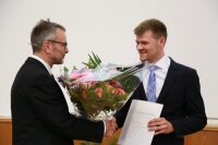 Der Dekan, Prof. Spielmann, überreicht die Blumen an den Preisträger M.Sc. Felix Wechsler (rechts).